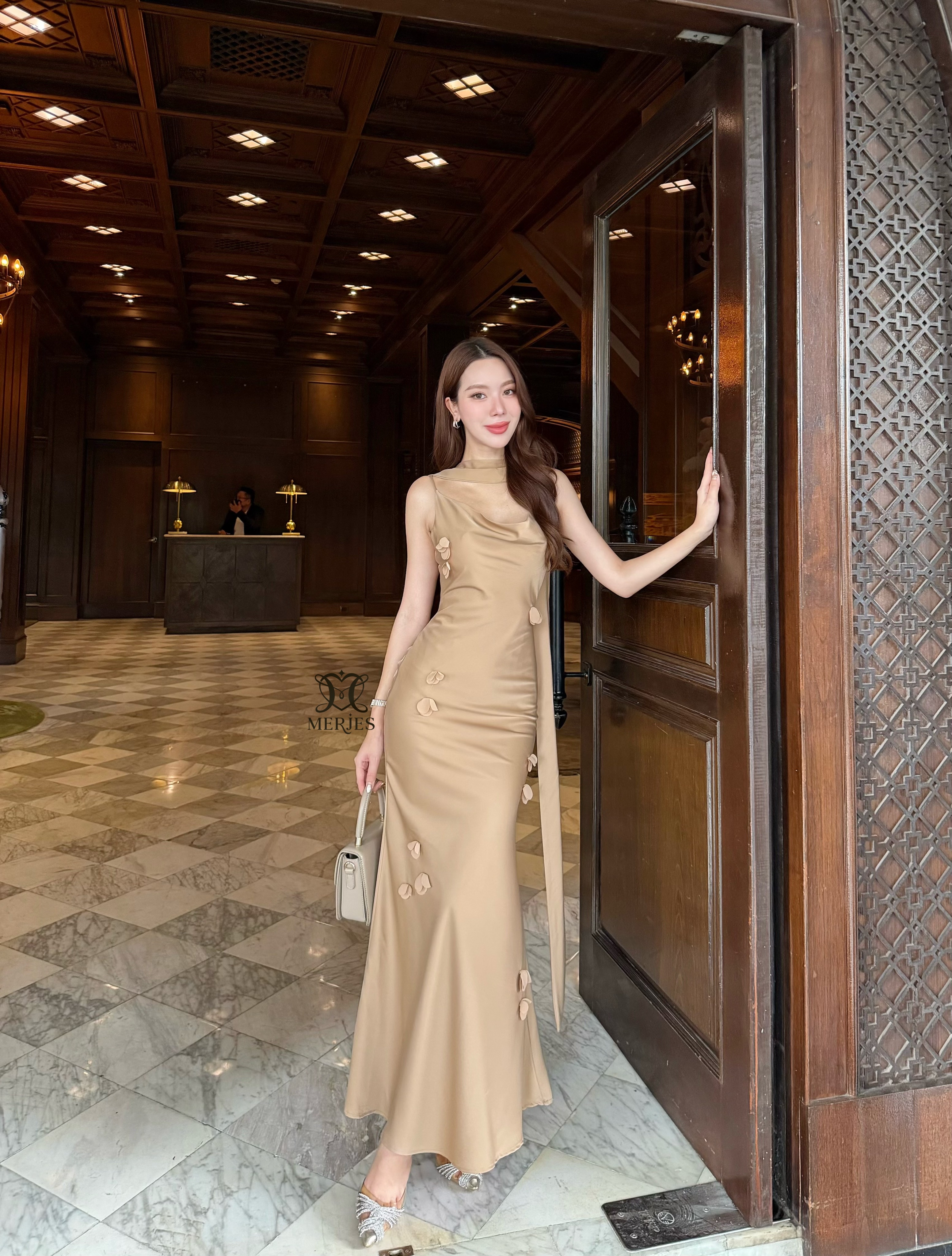 𝐌𝐄𝐑𝐉𝐄𝐒 𝐒𝐓𝐔𝐃𝐈𝐎 (เมอร์เจส) 𝐃𝐞𝐭𝐚𝐢𝐥 : เดรสยาวสีน้ำตาลทองผ้าซาตินสายเดี่ยวเข้ารูปสายสามารถปรับได้แต่งดีเทลด้วยดอกไม้