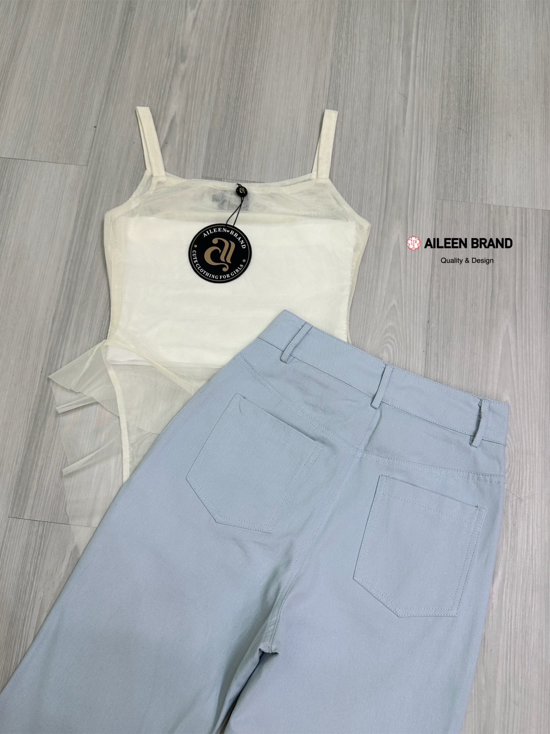 Set 2 ชิ้น เสื้อสายเดี่ยวเนื้อผ้าซีทรูอกเหลี่ยมแขนกุดทรงพอดีตัว ( ไม่เสริมฟองน้ำไม่มีซิปหลัง ) ชายแต่งปล่อยชายเฉียงเป็นระบายทั้งด้านหน้าและด้านหลัง มีเกาะอกสีขาวซับในแยกชิ้นให้อีกชิ้น มาพร้อมกับกางเกงขายาวเอวสูงสีฟ้าอมเทากระดุมและซิปด้านหน้า มีกระเป๋าล้วง