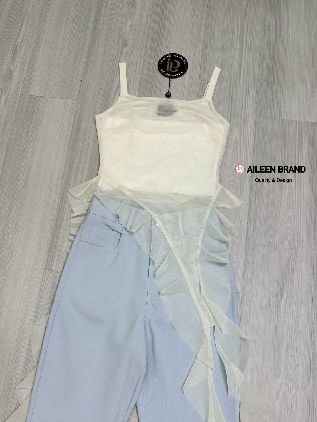 Set 2 ชิ้น เสื้อสายเดี่ยวเนื้อผ้าซีทรูอกเหลี่ยมแขนกุดทรงพอดีตัว ( ไม่เสริมฟองน้ำไม่มีซิปหลัง ) ชายแต่งปล่อยชายเฉียงเป็นระบายทั้งด้านหน้าและด้านหลัง มีเกาะอกสีขาวซับในแยกชิ้นให้อีกชิ้น มาพร้อมกับกางเกงขายาวเอวสูงสีฟ้าอมเทากระดุมและซิปด้านหน้า มีกระเป๋าล้วง