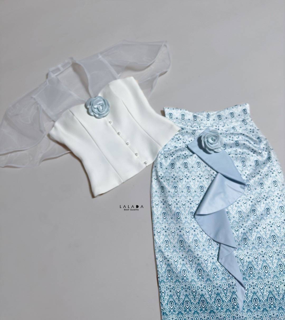 set 2 ชิ้นเสื้อสีขาวกระดุมหน้า ตัดเย็บอย่างดีมีซับใน + กระโปรงผ้าถุงสำเร็จทรงเอวสูง ผ้าพิมพ์ลาย แต่งระบายด้านหน้า+ เข็มกลัดดอกไม้ 2 ชิ้นติดได้ตามต้องการ