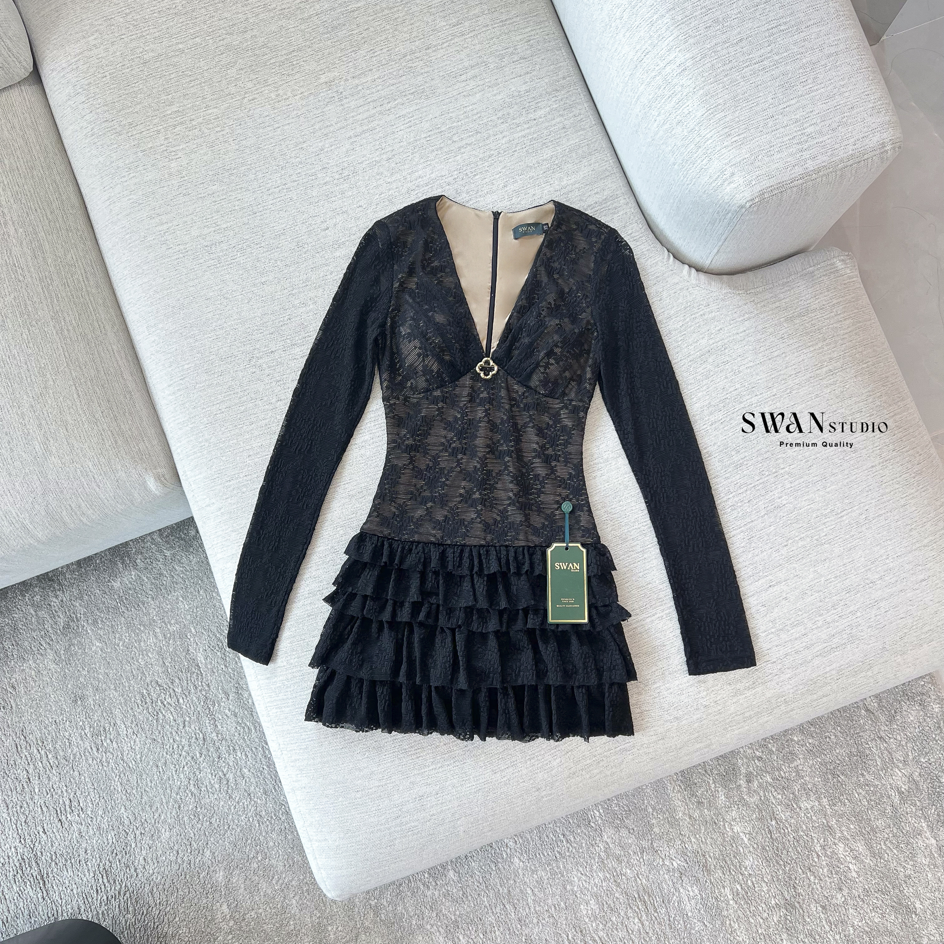 เดรสลูกไม้สีดำแขนยาวซีทรูซ้อนซับสีเนื้อ ดีไซน์เข้ารูปช่วงตัวคอวีลึกแต่งเข็มกลัดสีทองช่วงอกเพิ่มความหรูหราตัดต่อกระโปรงสั้นบานระบายเลเยอร์ชั้นๆด้วยผ้าลูกไม้ดูพริ้วหวานแฝงความเซ็กซี่ลงตัวเหมาะกับลุคดินเนอร์หรือออกงานกลางคืนที่ต้องการความโดดเด่นและดูแพง