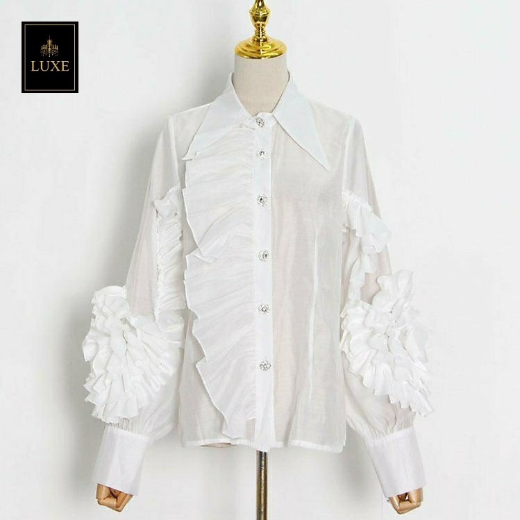 Label : LUXE เสื้อเชิ้ตคอปกแหลมแขนยาว ผ่าหน้าติดกระดุมเพชร สาบเสื้อแต่งระบาย ดีเทลแขนเสื้อแต่งด้วยผ้าในตัวเป็นรูปดอกไม้ ทำจากผ้าไหมเครปผสม เนื้อนุ่ม โปร่ง เบาสบายแต่ให้ความเป็นทรง
