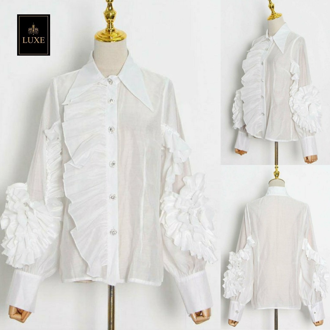 Label : LUXE เสื้อเชิ้ตคอปกแหลมแขนยาว ผ่าหน้าติดกระดุมเพชร สาบเสื้อแต่งระบาย ดีเทลแขนเสื้อแต่งด้วยผ้าในตัวเป็นรูปดอกไม้ ทำจากผ้าไหมเครปผสม เนื้อนุ่ม โปร่ง เบาสบายแต่ให้ความเป็นทรง