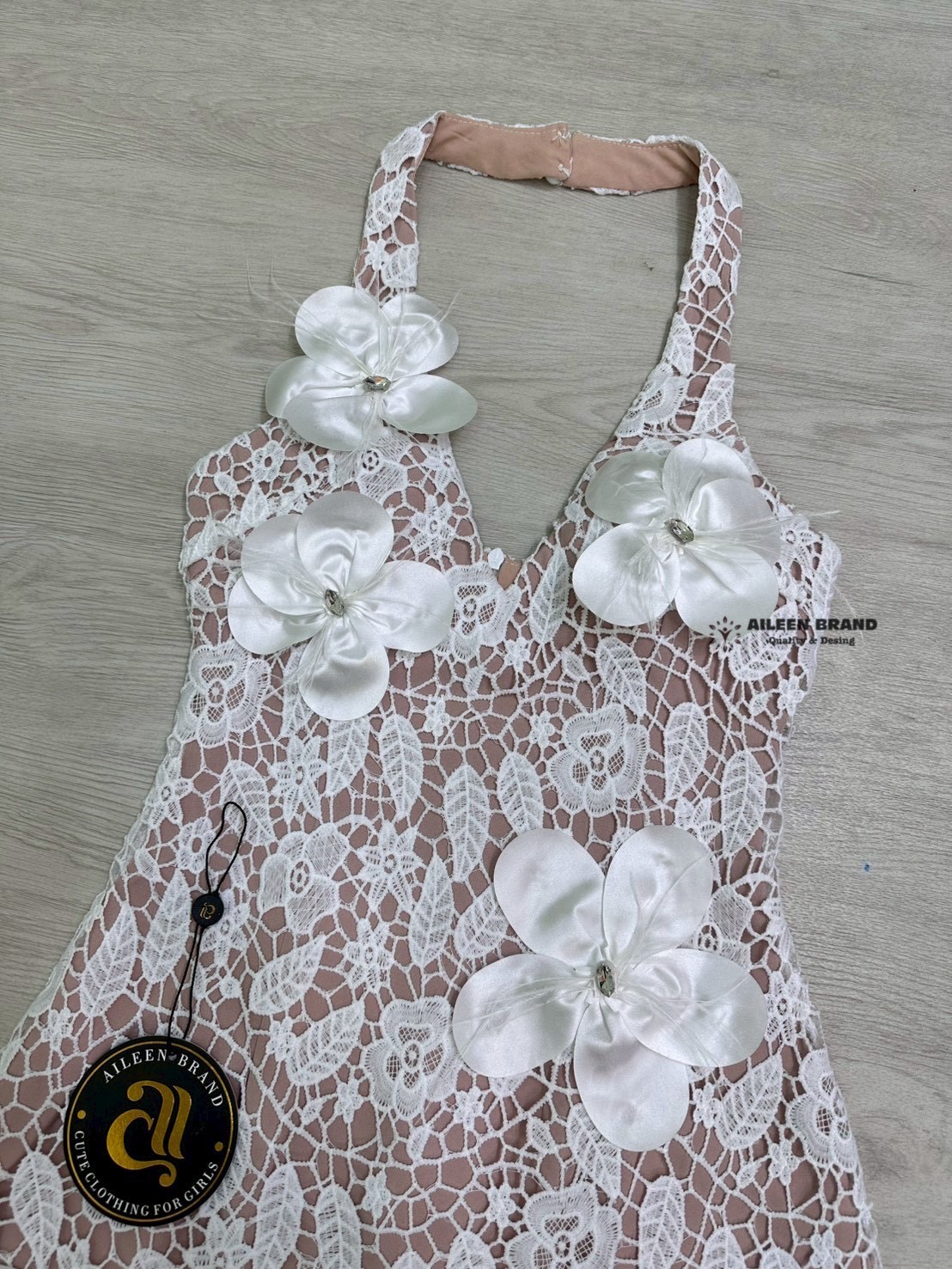 มินิเดรสคล้องคอ ช่วงอกเสริมฟองน้ำ งานเนื้อผ้าฉลุลูกไม้สีขาว ตัดกับชับในสีเนื้อ ดีเทลแต่งดอกไม้3D แซมด้วยขนนกและเพชร ด้านหน้า ปลายชายกระโปรงแต่งยั๊ก (ซิปหลัง)