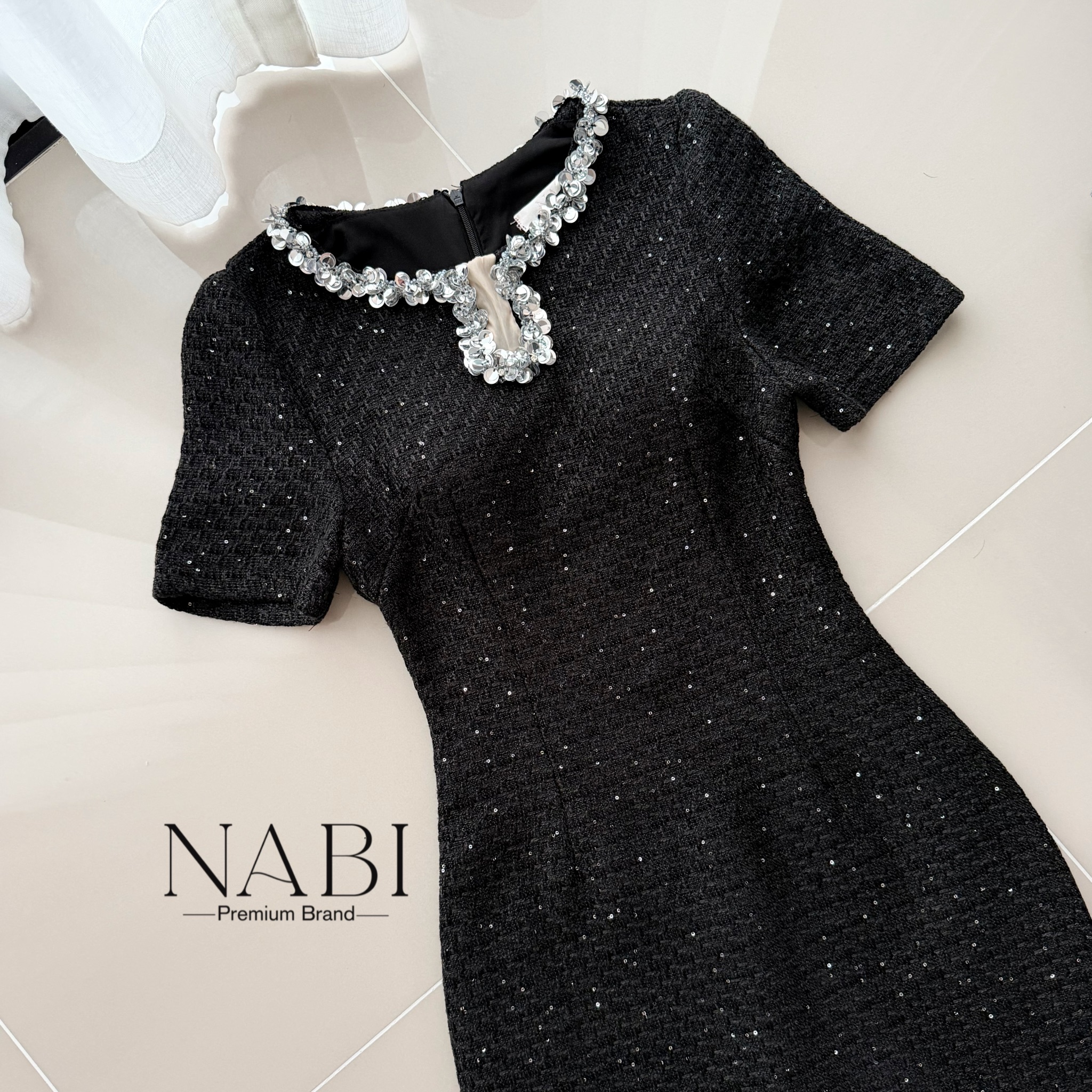 ชุดเดรสทรงเชฟเข้ารูปแขนสั้น ความยาวมิดเข่า ดีไซน์คอกลมตกแต่งมุกคลิตเตอร์เป็นแถบล้อมรอบคอ และแต่งผ้าซีทรู ใช้ผ้าทวีดเนื้อหนาที่มีพื้นผิว ประดับด้วยเม็ดกลิตเตอร์เล็กทั่วผืน ให้ประกายเป็นจุด ๆ เรียบแต่หรูดูแพง มีซับในและฟองน้ำ งานซิปซ่อนด้านหลัง ผ่าด้านหลัง