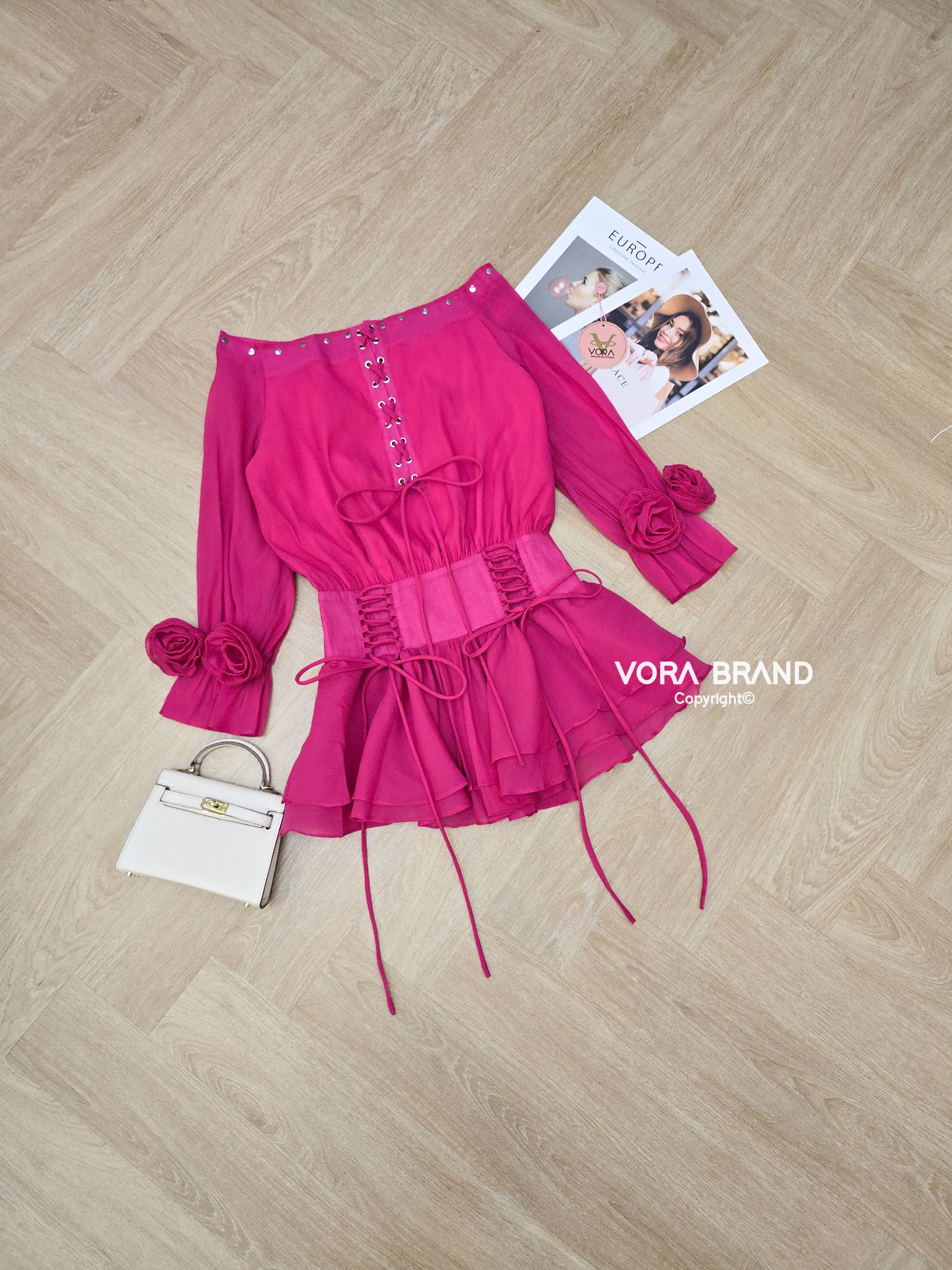 Dress สั้นปาดไหล่แขนยาวสม็อคบานปลายแขน แต่งเข็มกลัดดอกไม้ปลายแขน ช่วงไหล่แต่งตอกหมุด ด้านหน้าแต่งร้อยเชือกไขว้ผูกโบว์ เอวเข้ารุป แต่งร้อยเชือกด้านหน้า ช่วงกระโปรงจับจีบระบาย2ชั้น
